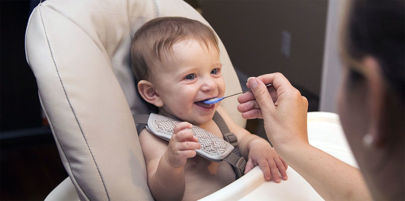 baby in high chair being fed with blue spoon