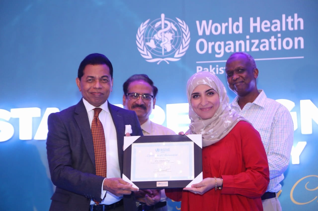 Four people on a stage, three men and a woman. The woman, Nada, is receiving a Certificate of Appreciation