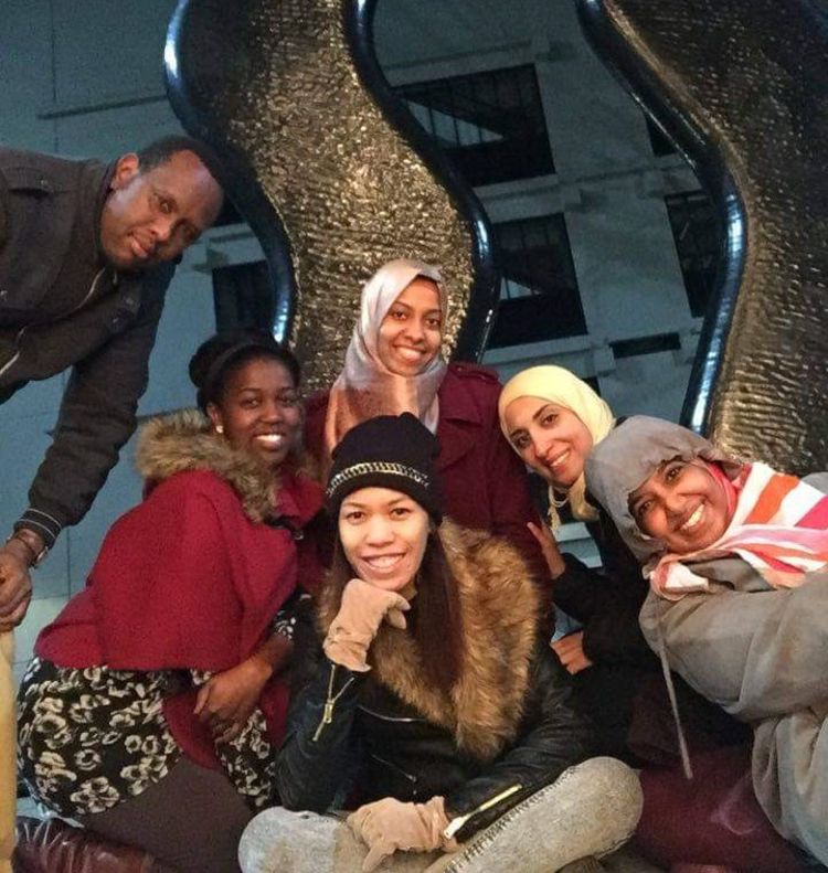 A group of people pose for a photo in front of A Sign for Art sculpture on campus