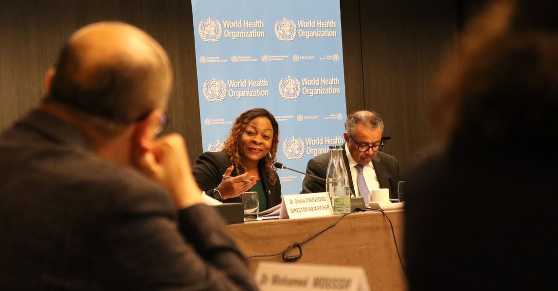 Woman and man with microphones at desk, in front of listeners