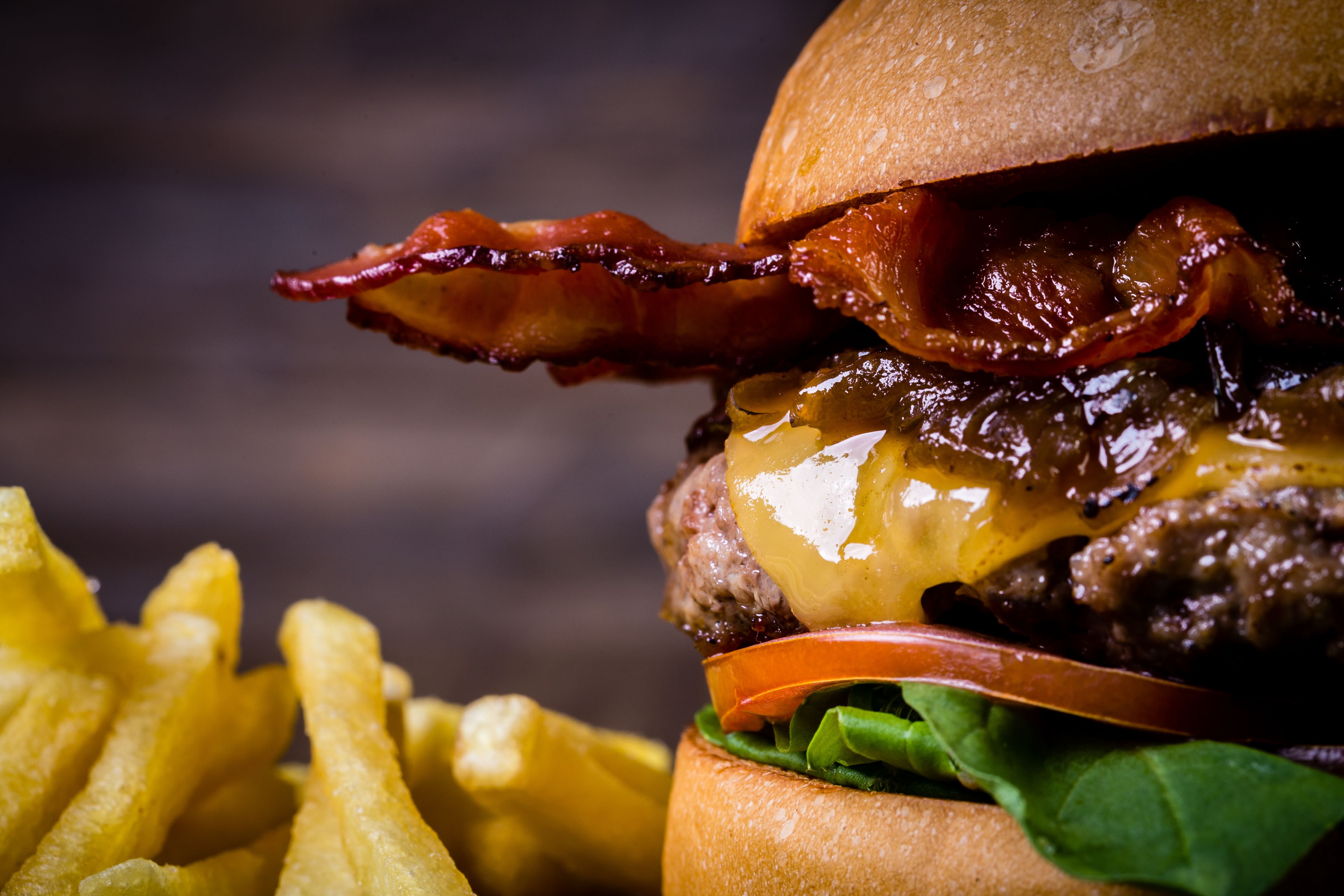 A meat beefburger with cheese, bacon, rocket leaves, tomatoes and caramelised onions, with French fries