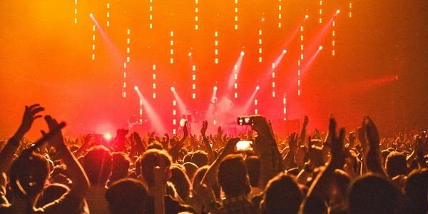 A crowd of people at a music concert facing a lit up stage.