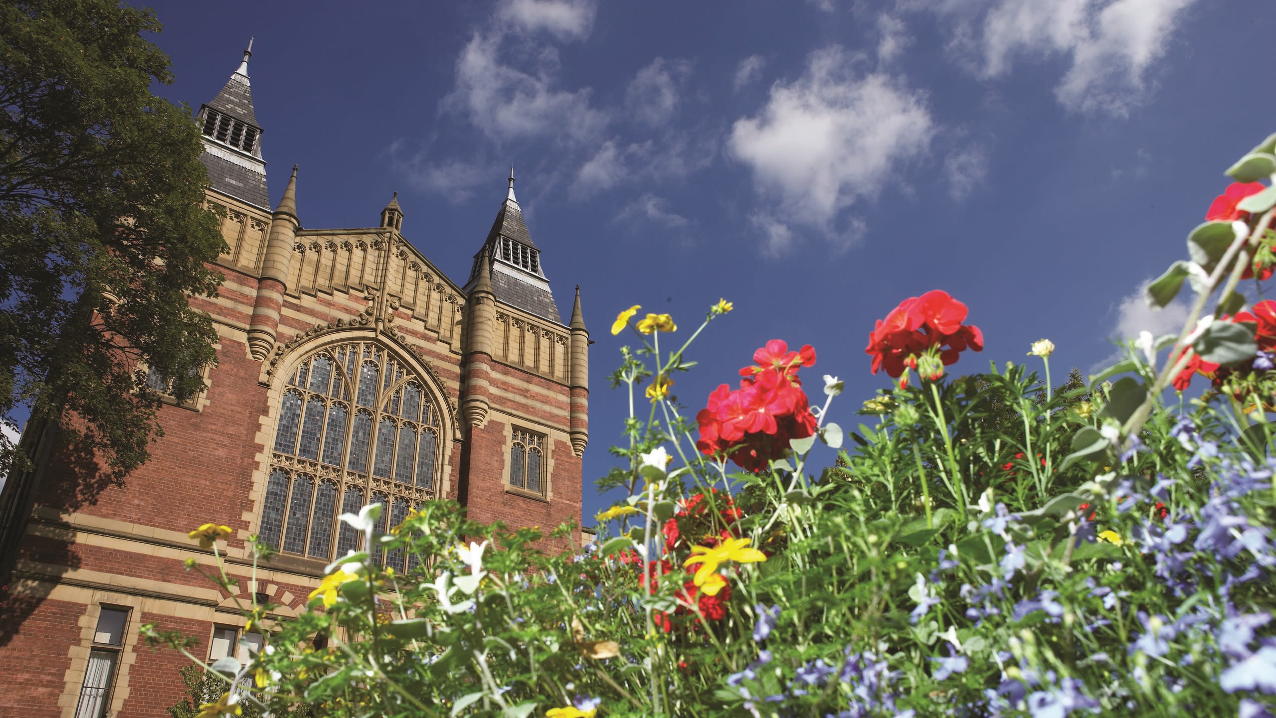 The Great Hall on a sunny day with blue sky and brightly coloured flowers growing in the foreground