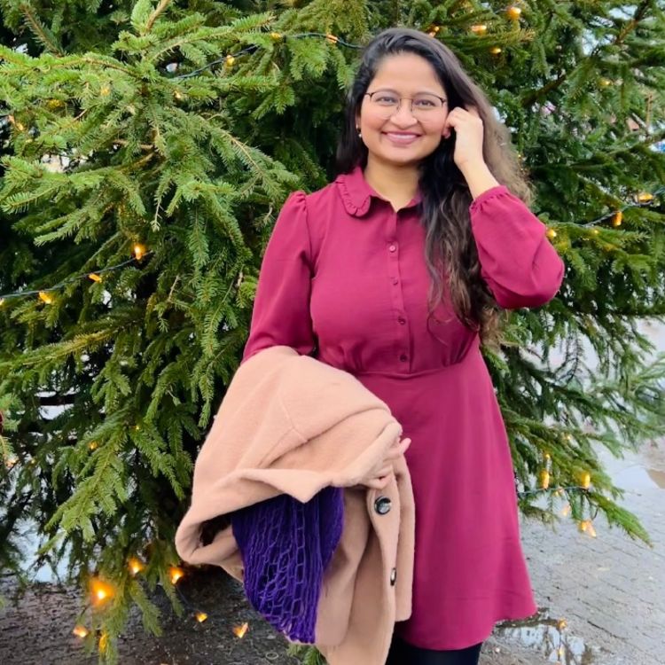 Photo of Priyanka Sonawane wearing a pink dress and stood in front of a christmas tree.