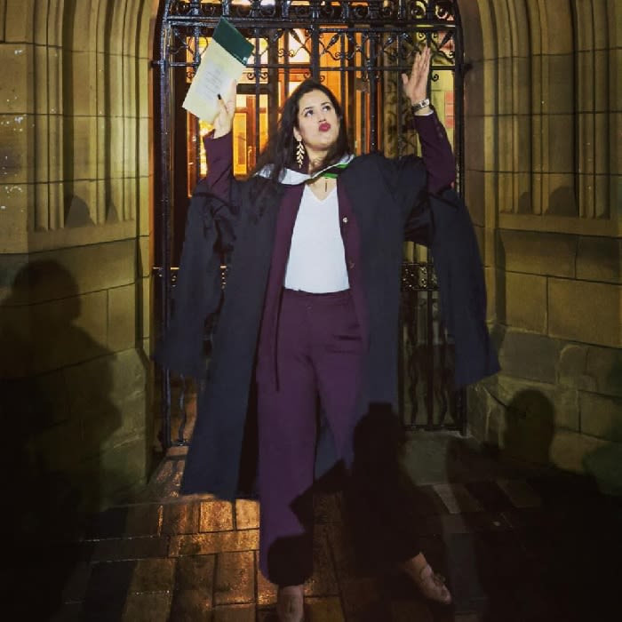 Image of Karishma Singh posing with her hands aloft in her graduation gown and hood.