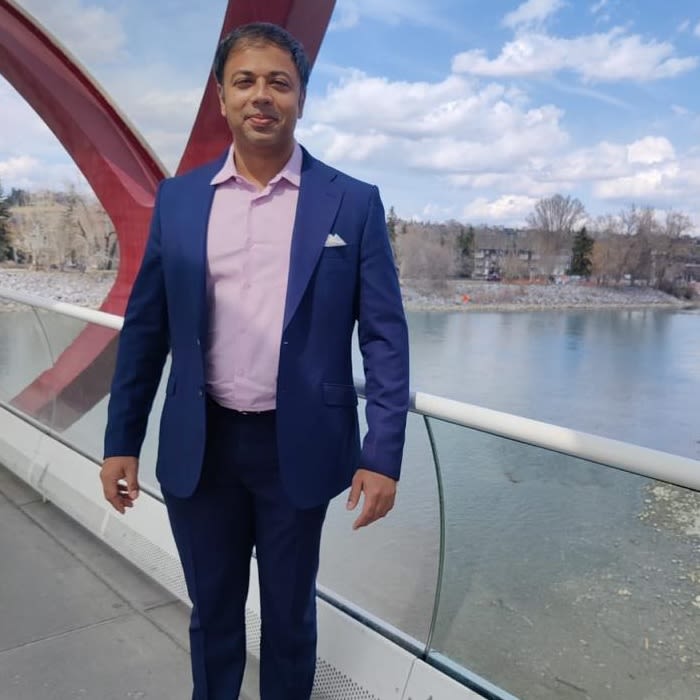 Photo of Varun Sanam wearing a blue suit and stood on a bridge over a river