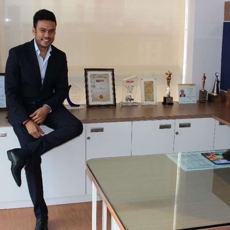 Aaryav Gupta sat in an office wearing a suit. Alongside a number of awards and certificates
