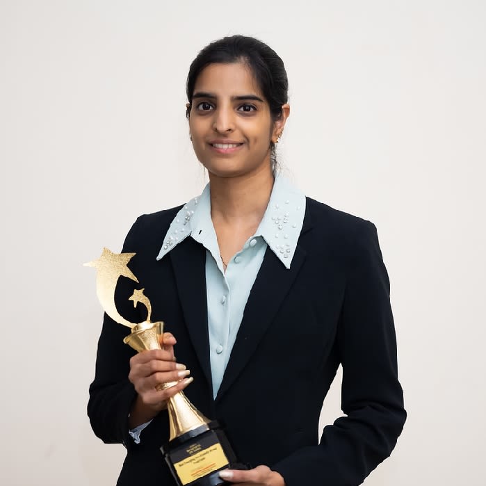 Photo of Vedashree Nadendla wearing a suit and posing with a trophy