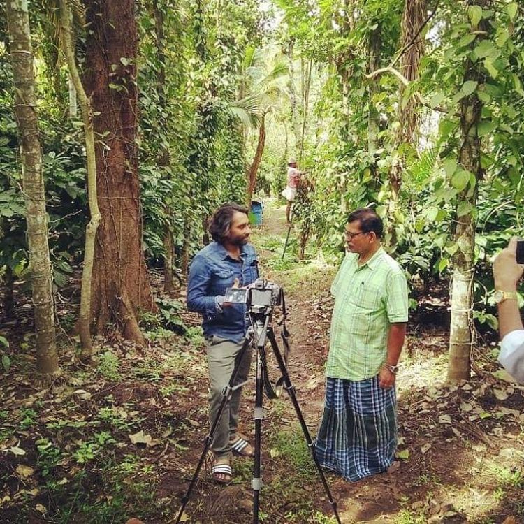 Photo of Anith Puthiyankath stood talking to another man in a forest, next to a camera on a tripod.