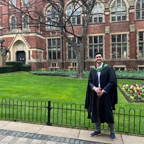 Photo of Anirudh Kulkarni wearing his graduation gown and hood, and stood in front the great hall at the university of leeds
