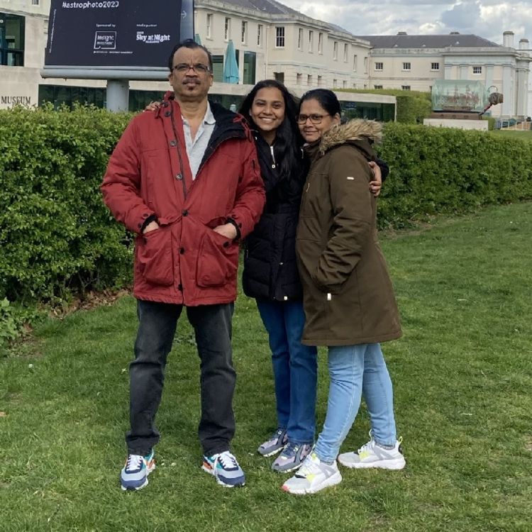 Profile picture of Gisel Fernandes. Three people stood on grass in front of a hedge and large white building