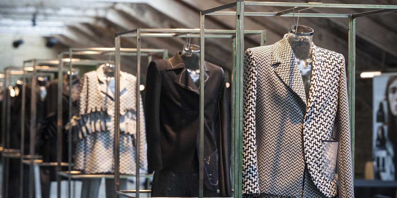 A row of black and white jackets and blazers hang in individual metal cubic frames.