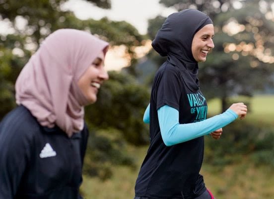 Namrah Shahid on the right smiling and running alongside another woman. Both are wearing hijabs.