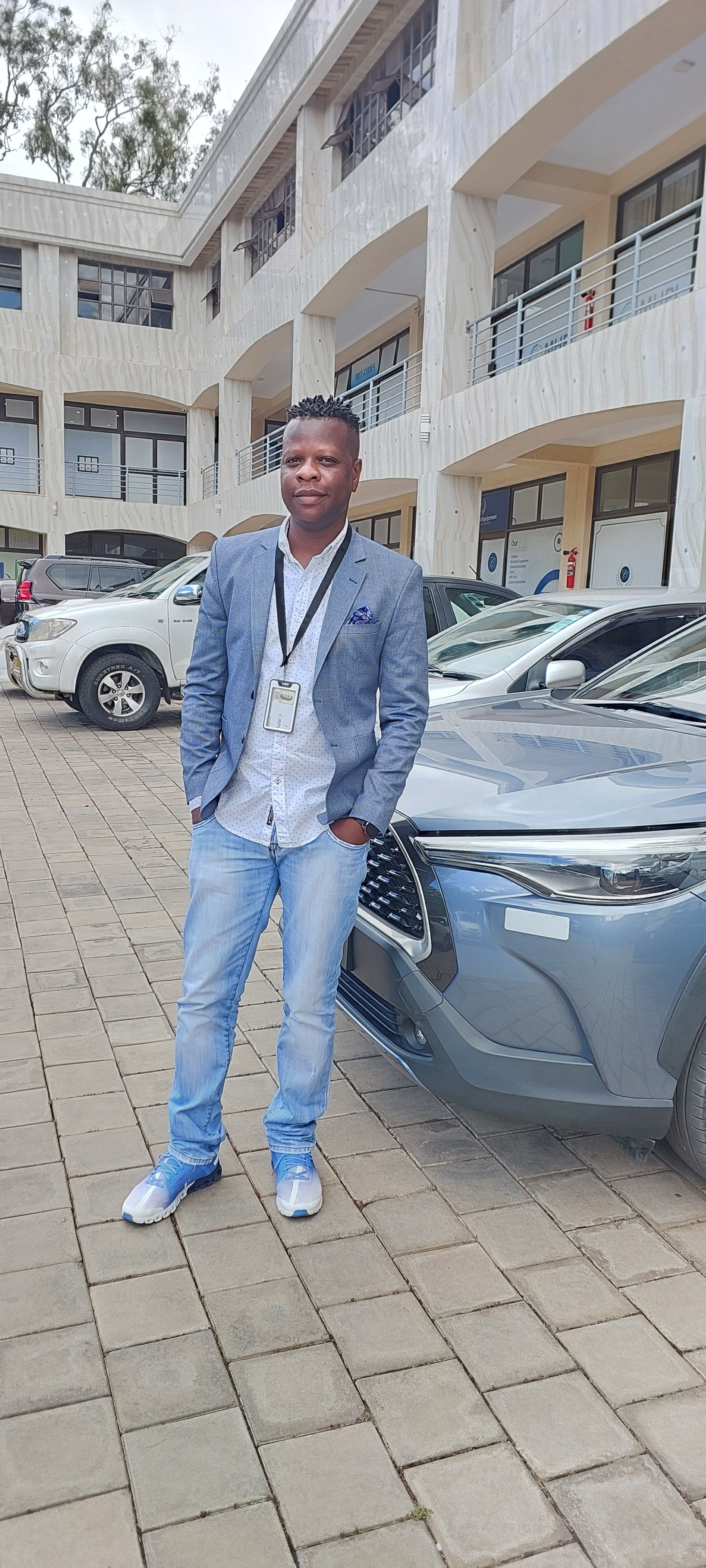 man standing in front of cars with hands in pocket