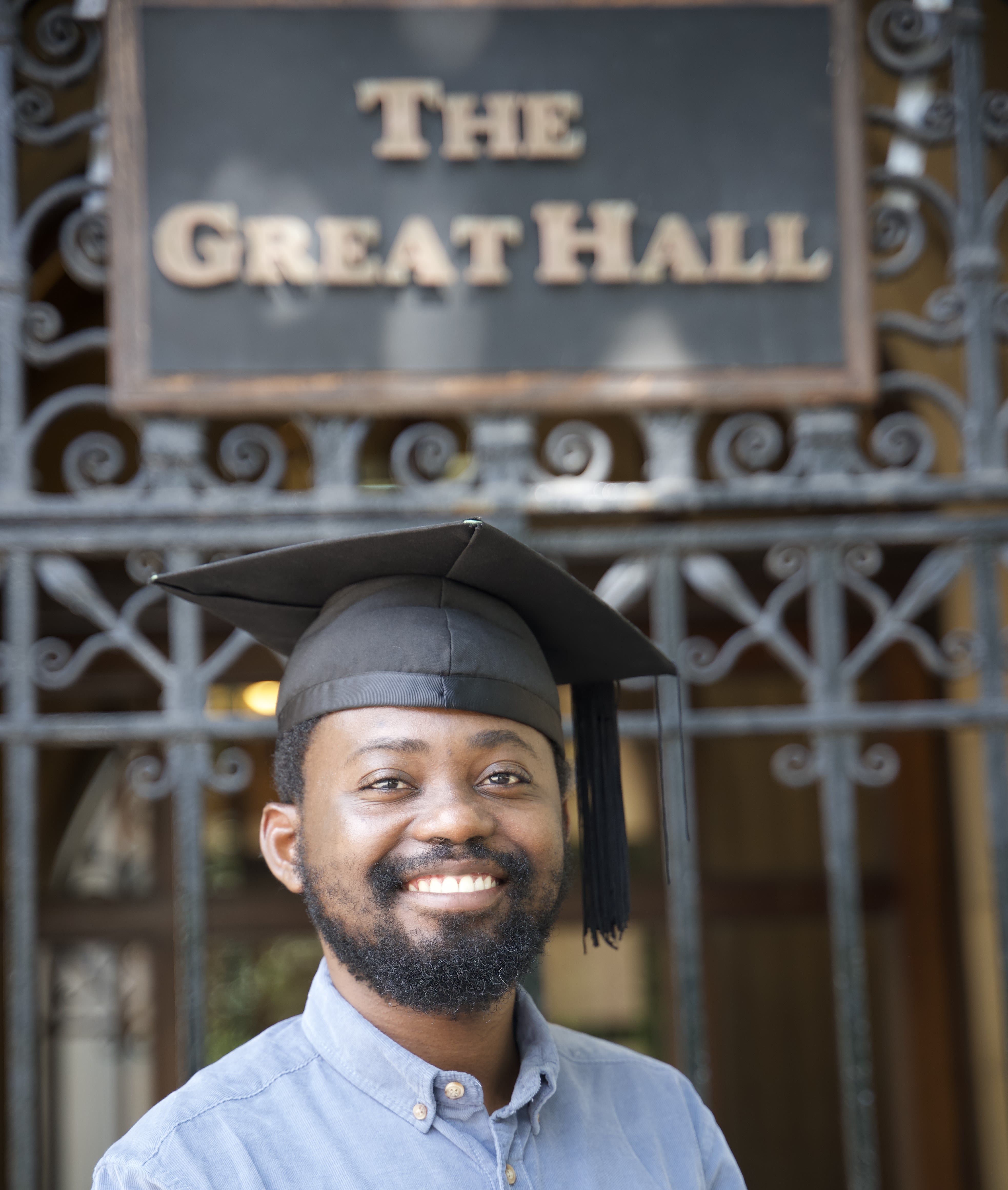 man wearing mortarboard standing in front of The Great Hall sign