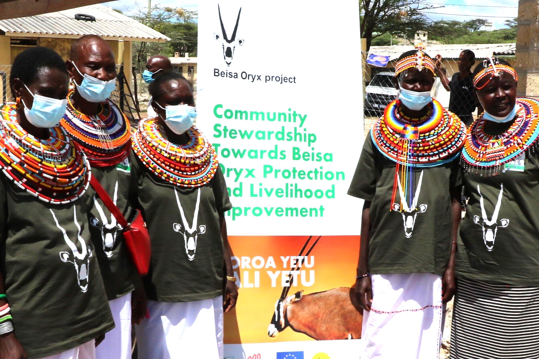 five people in face masks standing around banner about oryxes