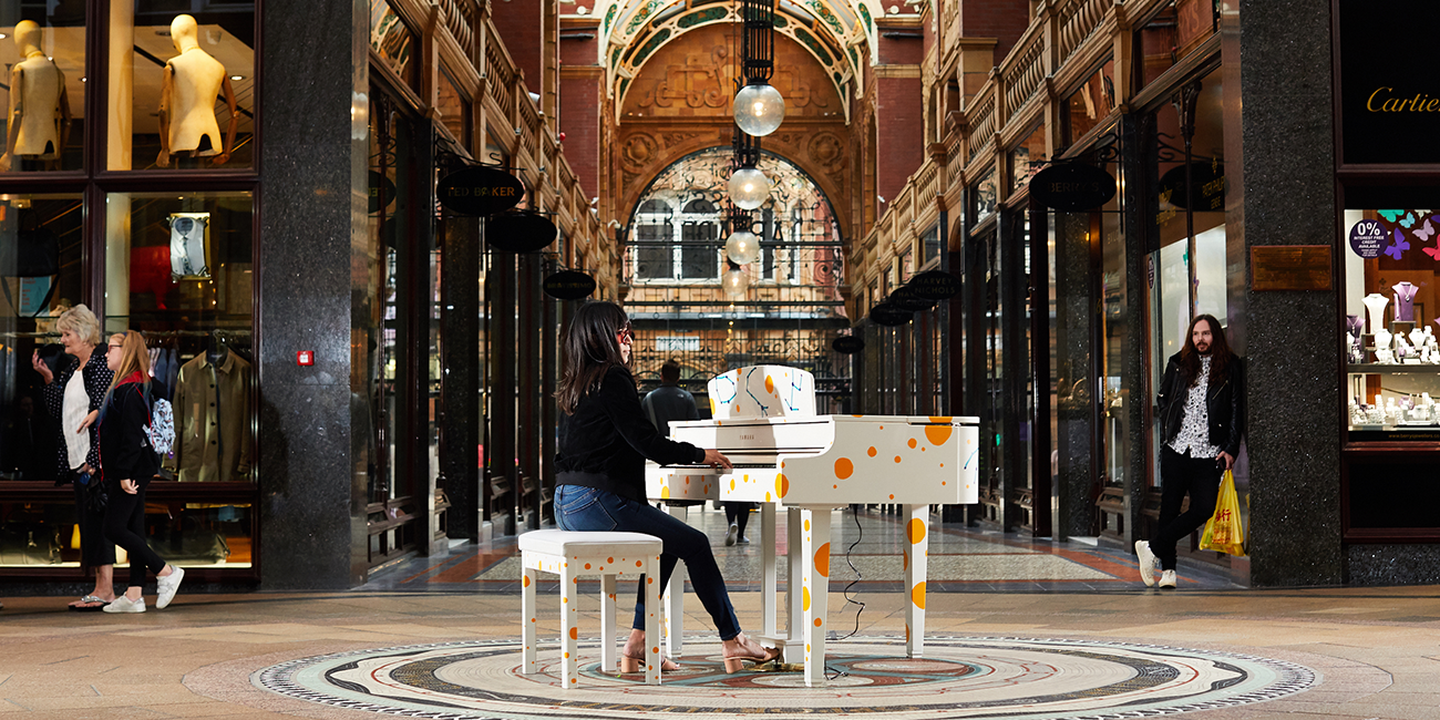 A person sits playing a white and orange piano in Victoria Quarter, Leeds.