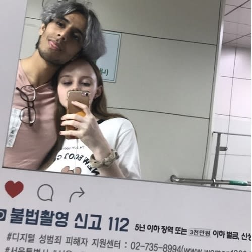 A man in a pink t-shirt and a woman in a white t-shirt pose for a photo taken using a mirror