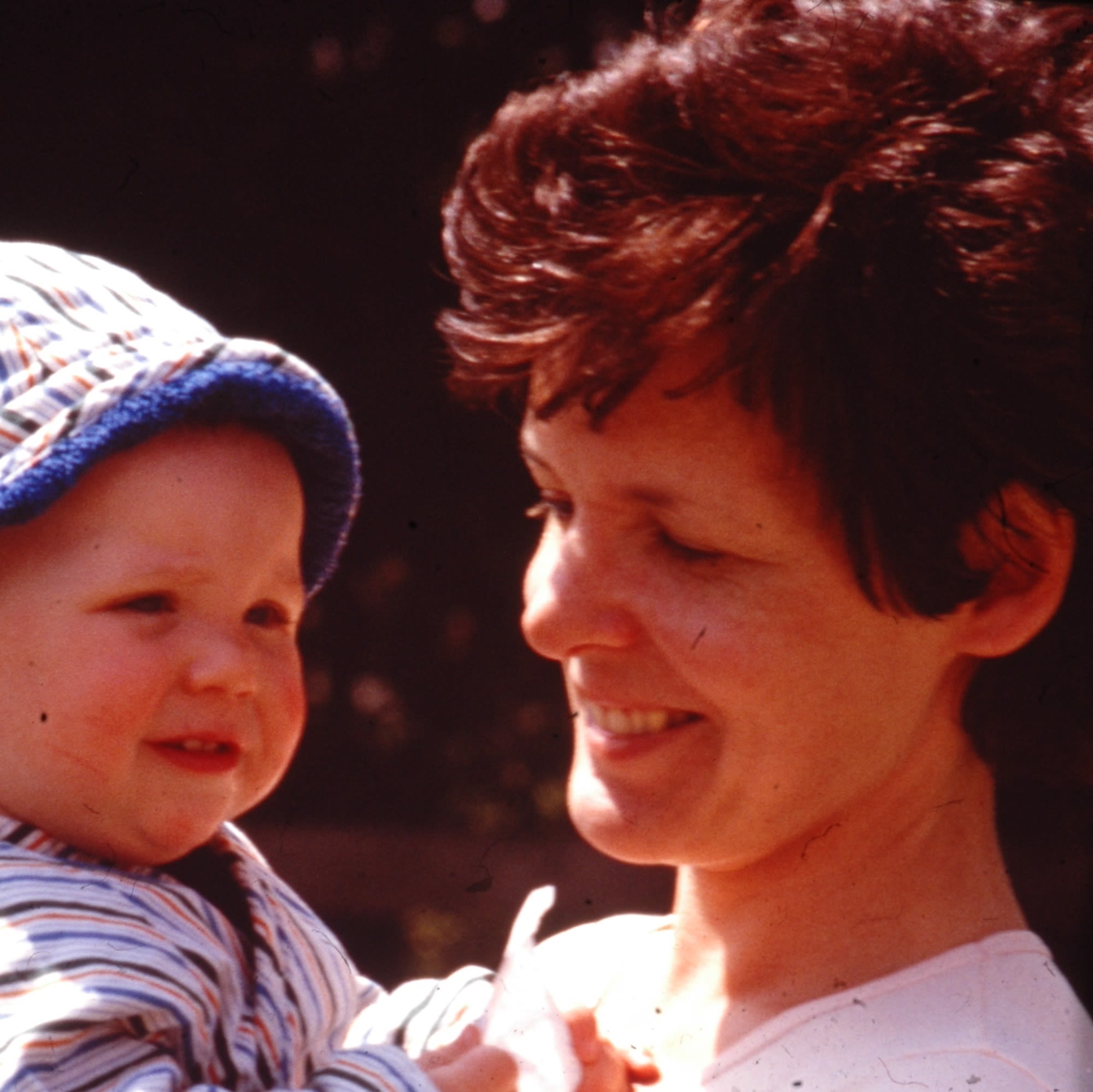 An old photo of a woman with short brown hair, smiling and holding a baby