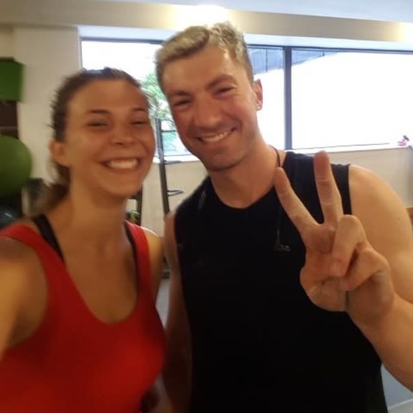 A man and woman in the gym pose for a photo. The man is holding up the peace sign