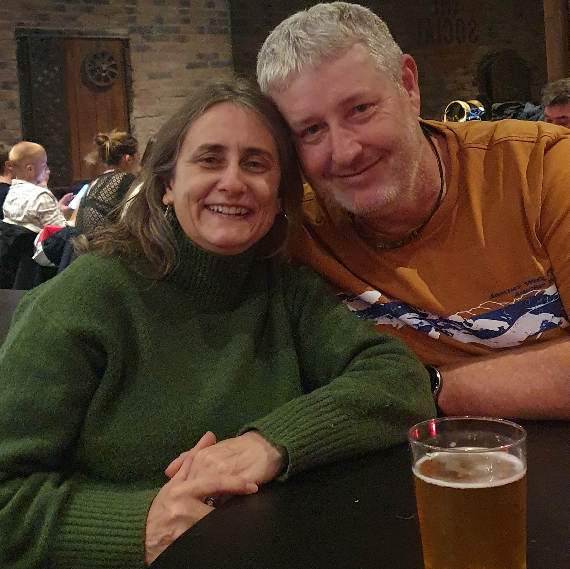 A man and a woman sat in a bar smiling for the camera