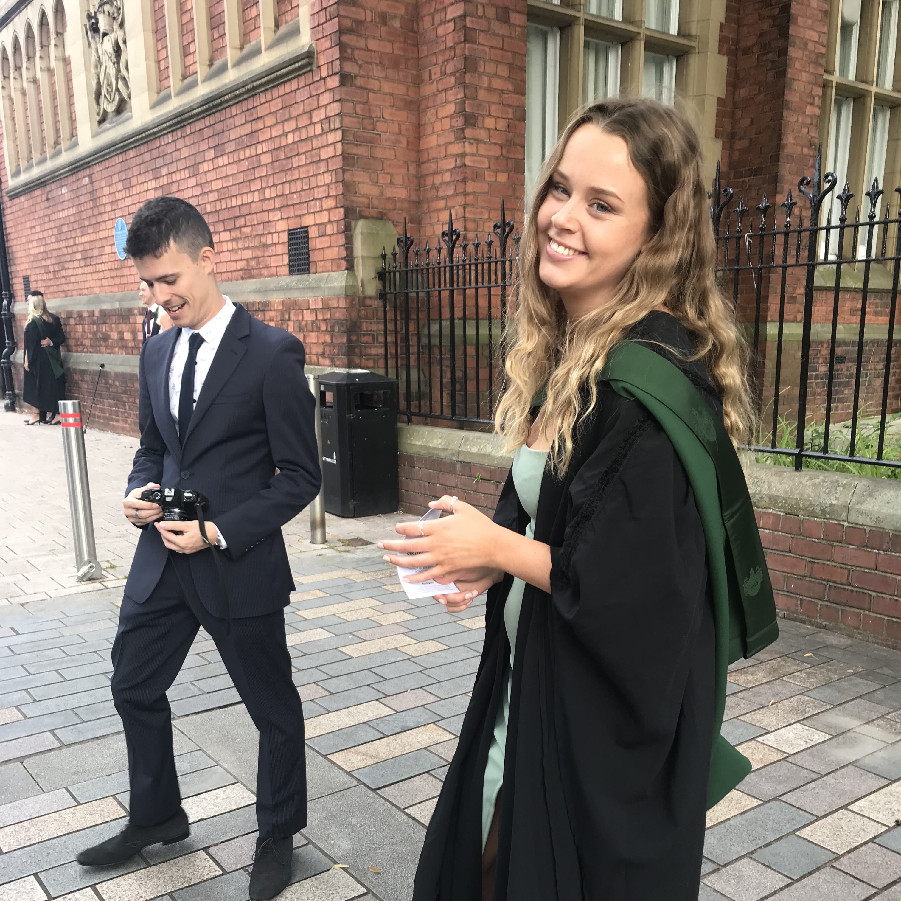 A man and a woman on graduation day outside the great hall. The man is wearing a suit, the woman is in a graduation gown