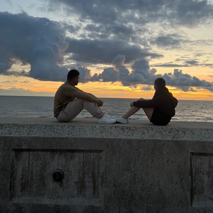 A man and a woman sat facing each other on a wall, looking out to the sea