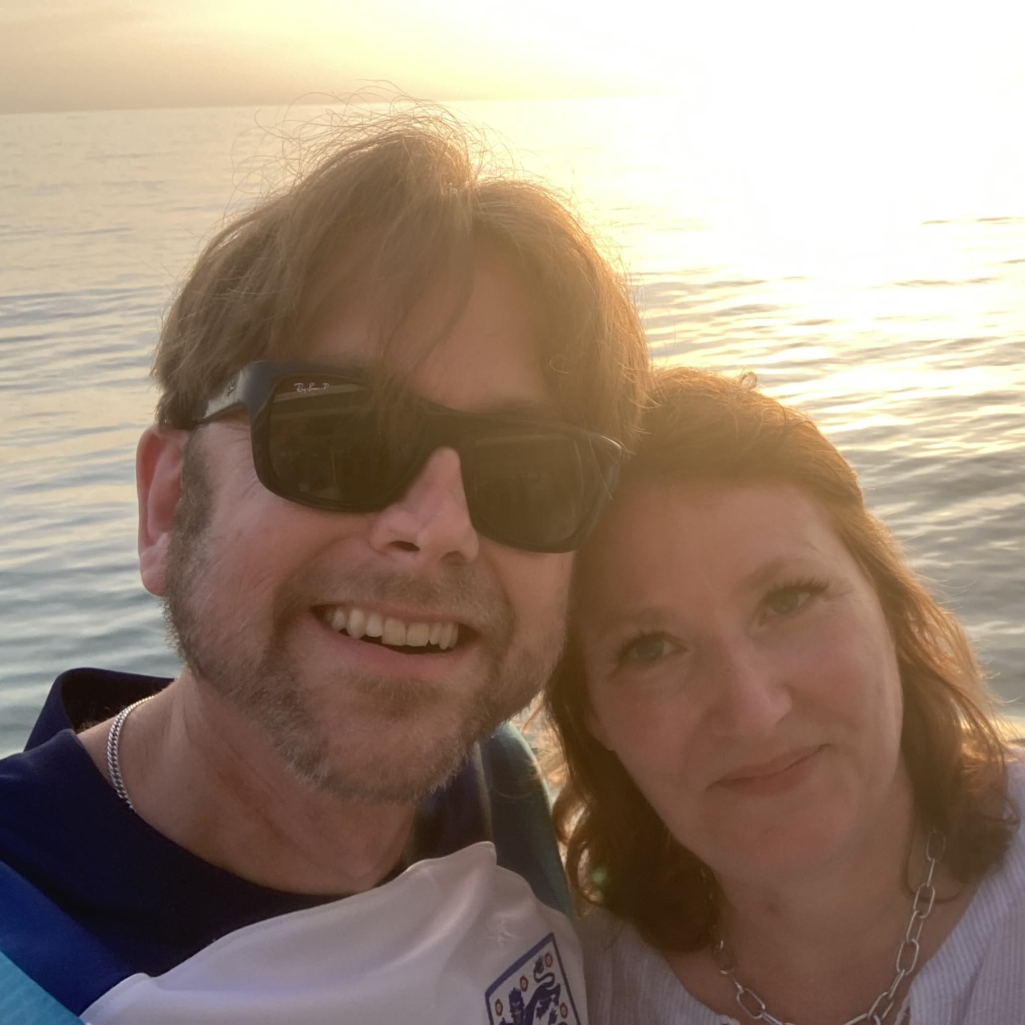 A man and a woman smiling for a photo with the sea and a sunset behind them