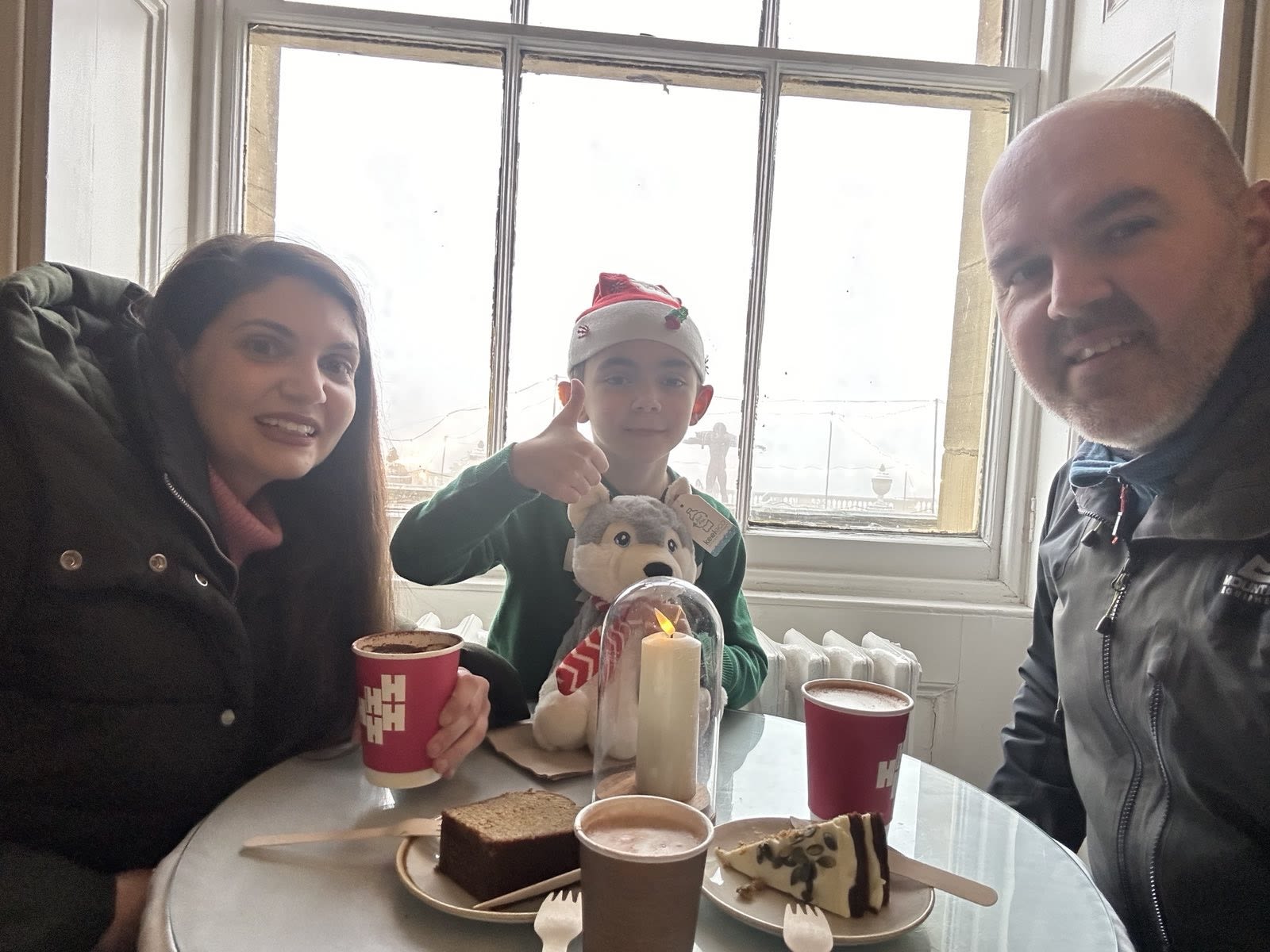A man, woman and boy sat around a table with hot drinks and cake
