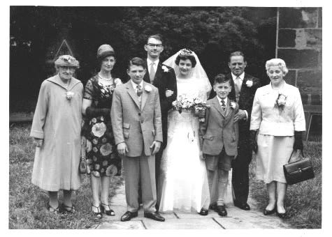 An old black and white photo of a man, woman and their families, on their wedding day