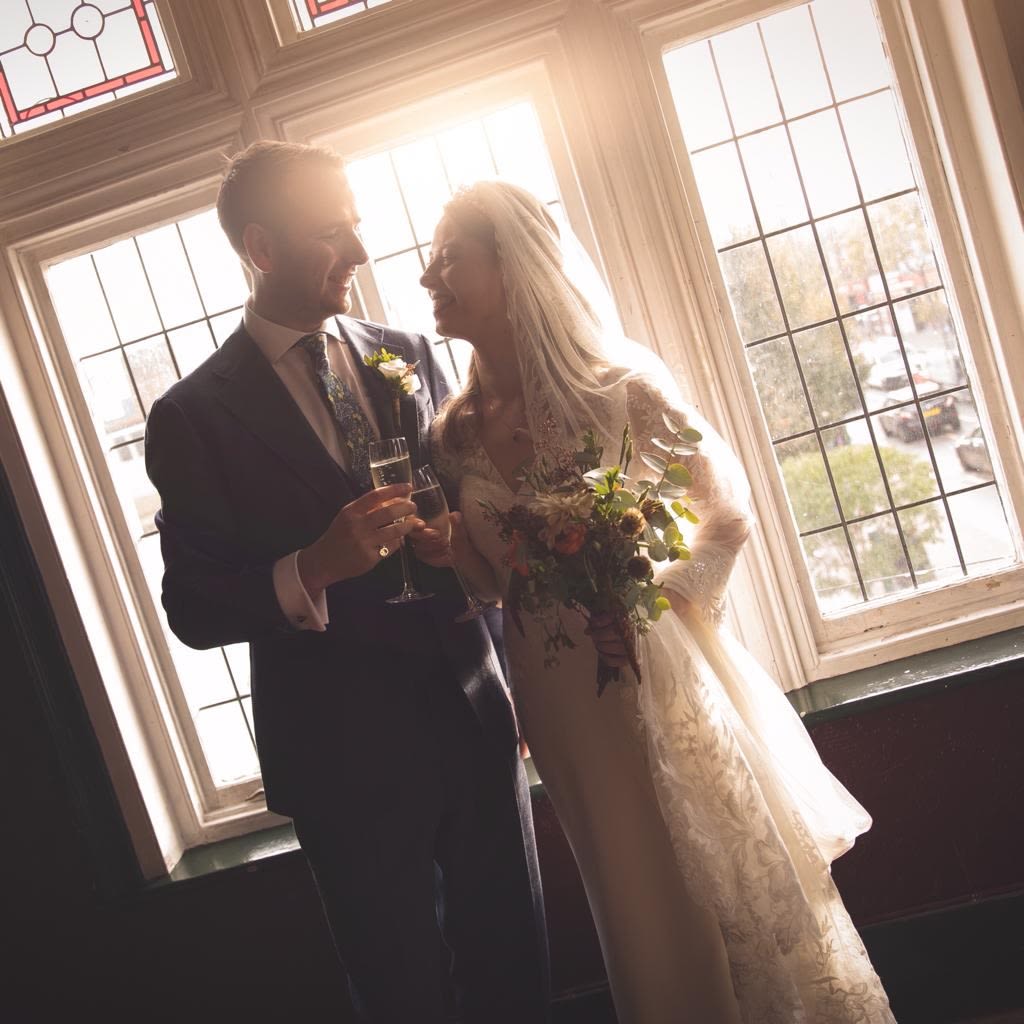 A man and woman on their wedding day standing by a stained glass window