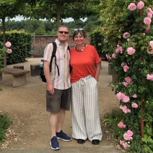 A man and woman pose for a photo next to a large rose bush