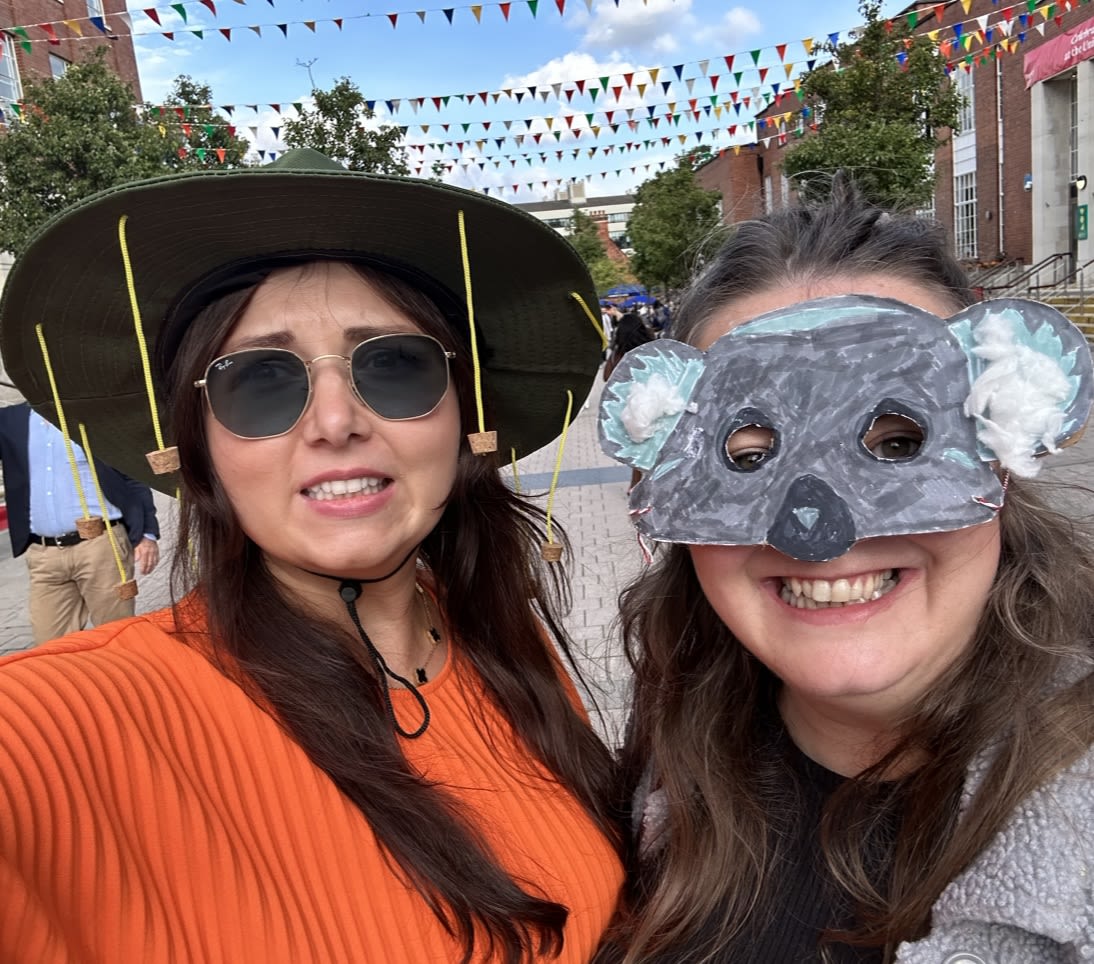 Two women smiling for the camera. One is wearing an owl mask, the other is wearing a cork hat