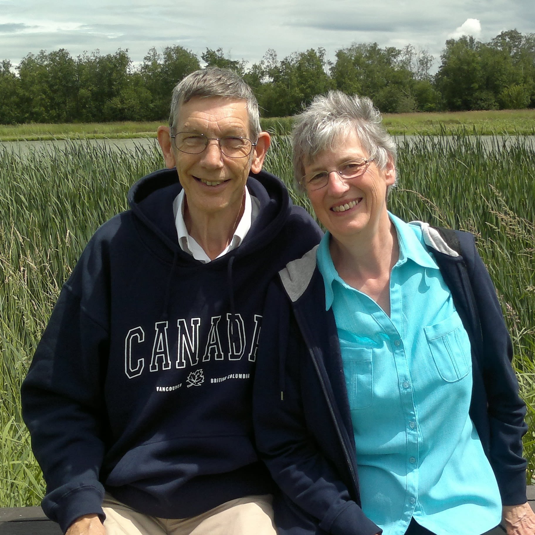 A man and woman are sat in front of some tall grass smiling for a photo