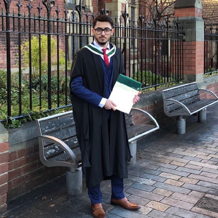 Photo of Haris Raja in his graduation gown and hood, holding his degree certificate