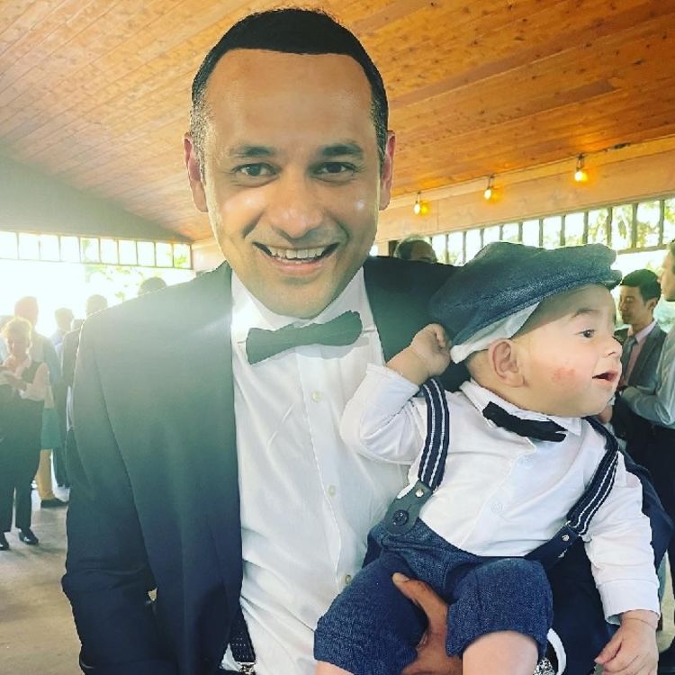 Photo of Salman Arif in shirt, blazer and bowtie, holding a baby