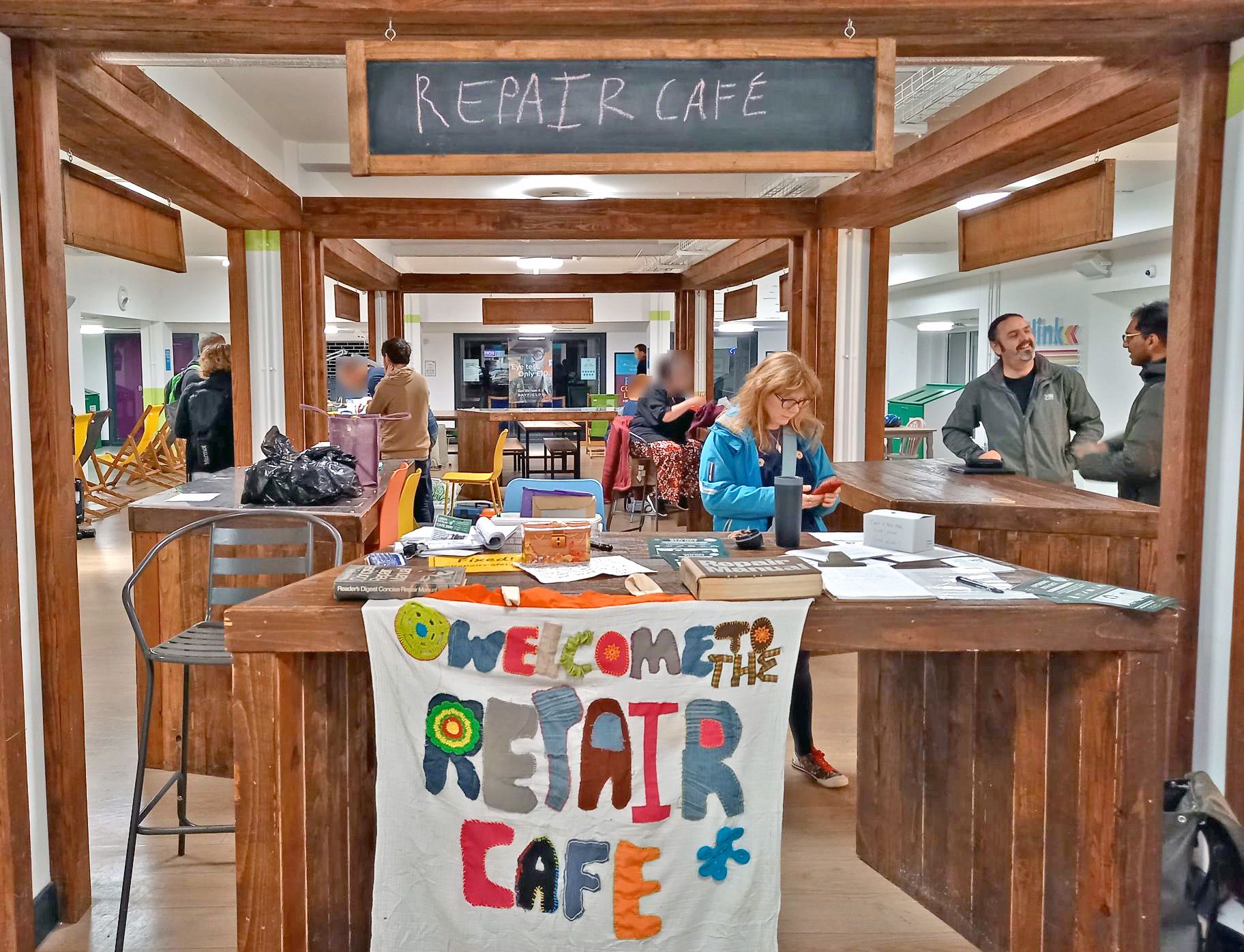 A wide view of a stall in the Leeds University Union, featuring a selection of items undergoing repair by the Leeds Repair Cafe team. There is also a range of reading material and manuals to support the activity.