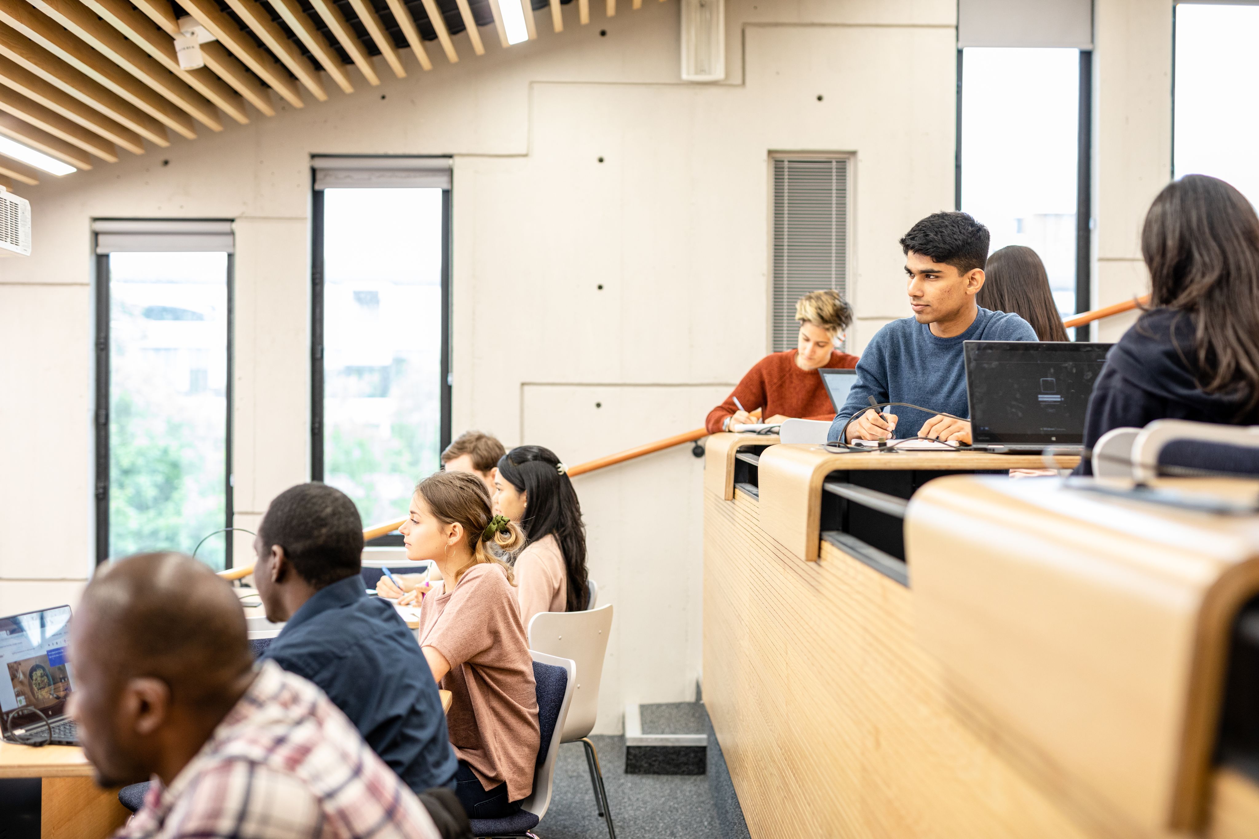 Two rows of students in a lecture theatre at the University of Leeds. The image focuses on a student in a blue top who has a laptop open in front of them.
