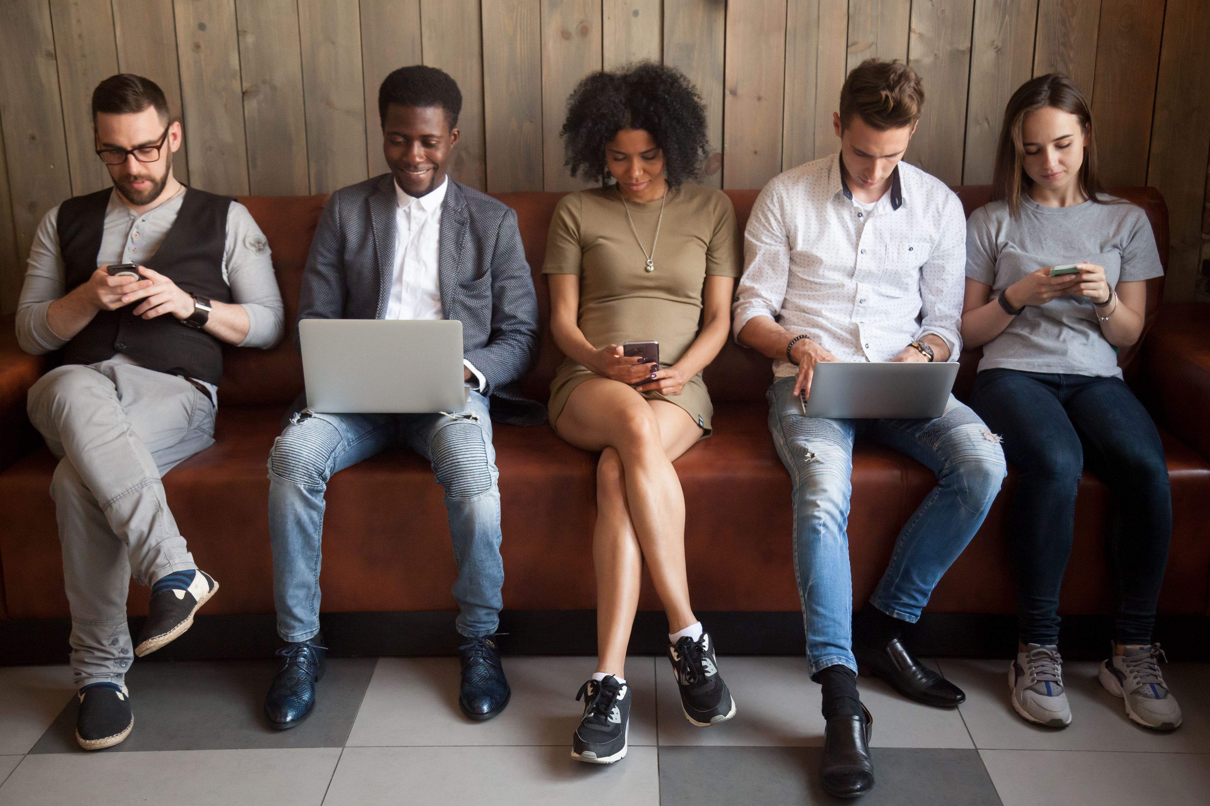 Five seated people, using a range of digital devices including mobile phones and laptops.