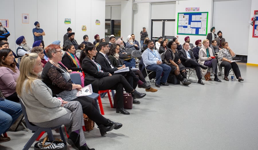 A room of people sat on chairs listening to someone presenting who is not in the photo