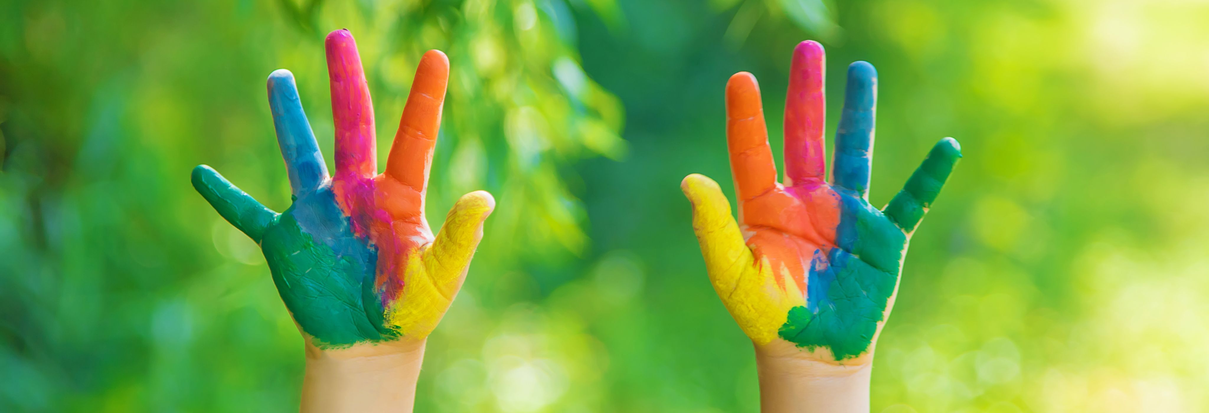 A pair of hands waving in sunlight, with the palms and fingers vividly painted in bright colours.
