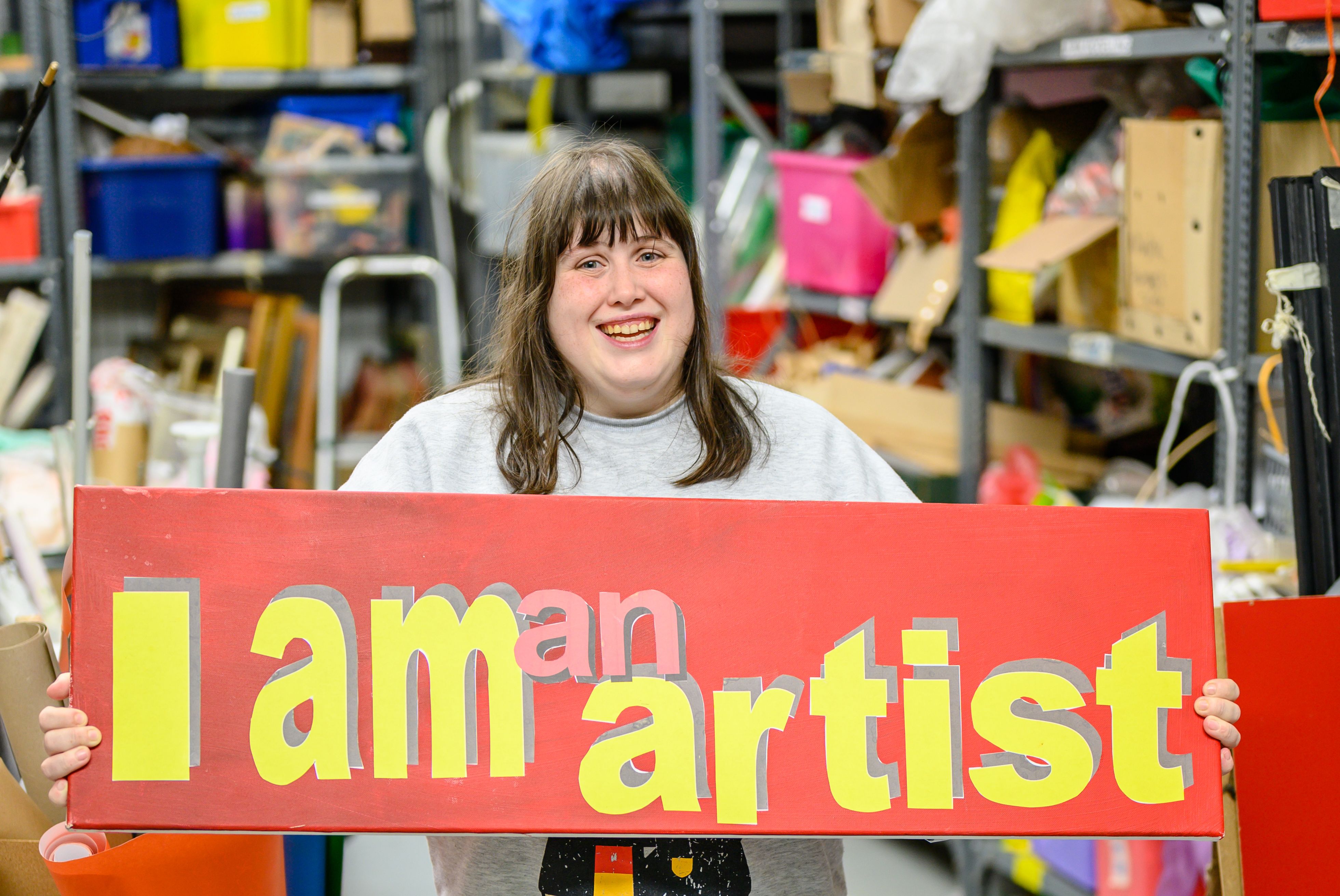Ella pictured holding a sign that reads: I am an artist.