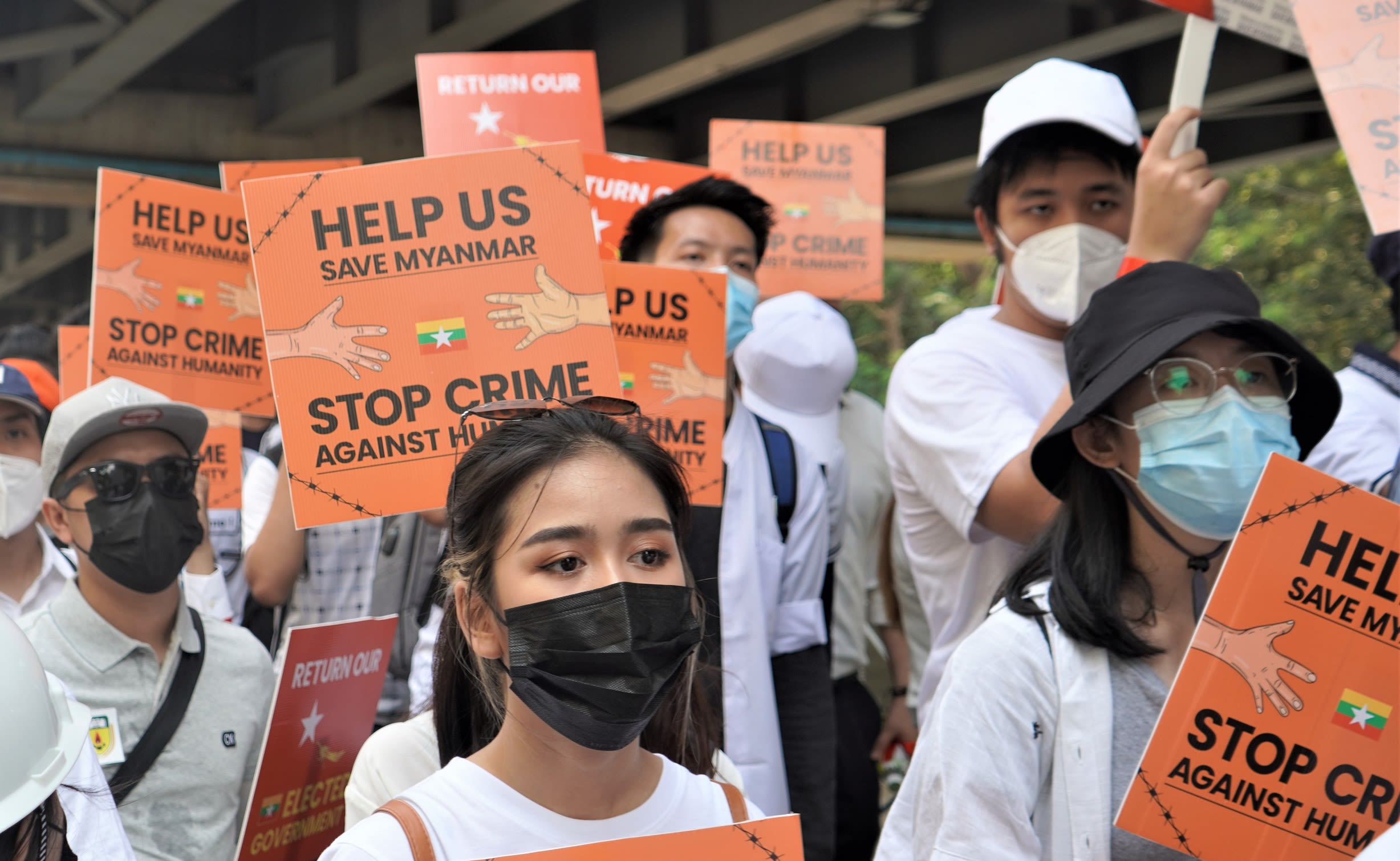 Protestors in face masks in Myanmar holding orange placards that say 'Help us save Myanmar. Stop crime against humanity'