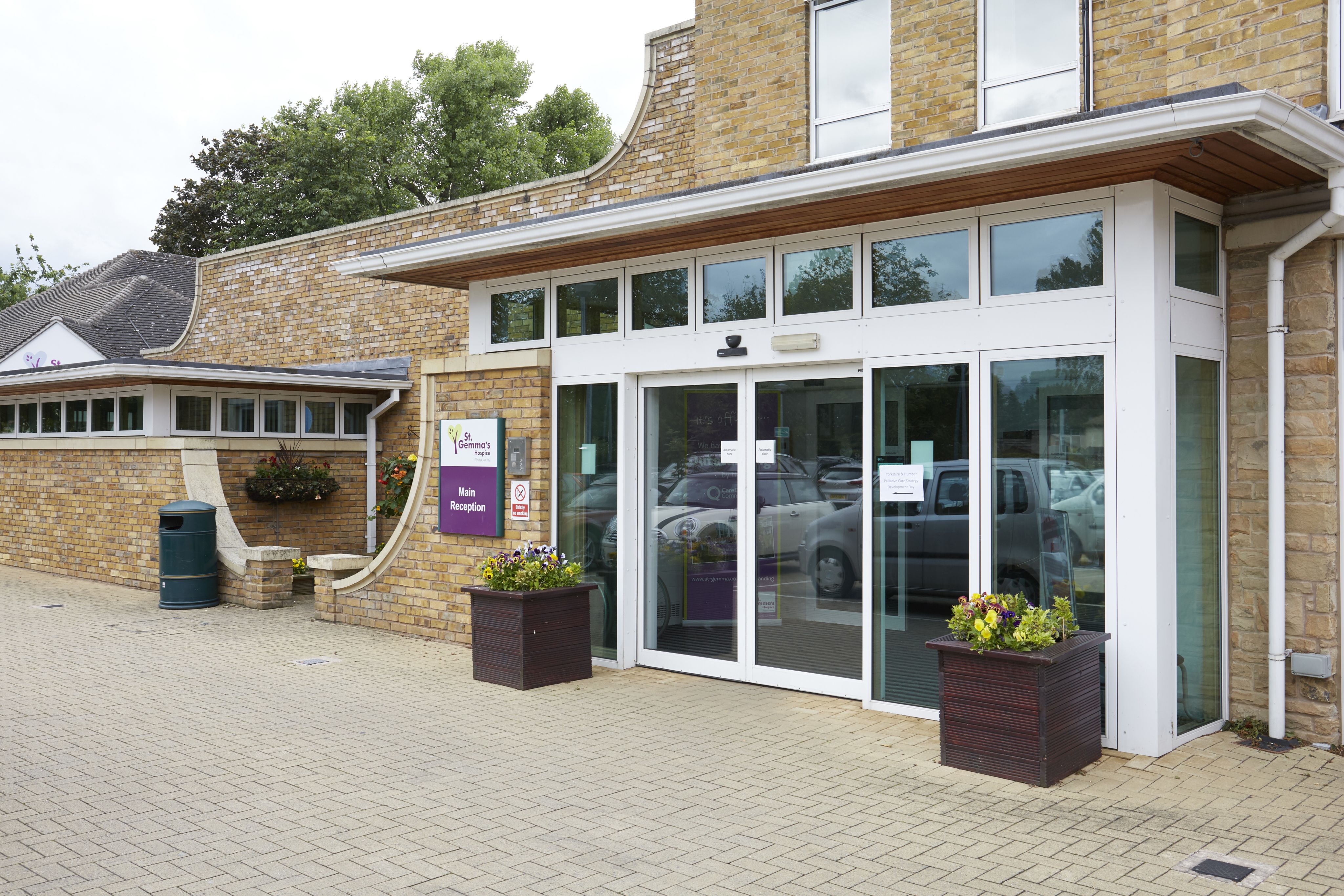 A glass fronted entrance to a building. A sign next to the door says St Gemma's Hospice Main Entrance