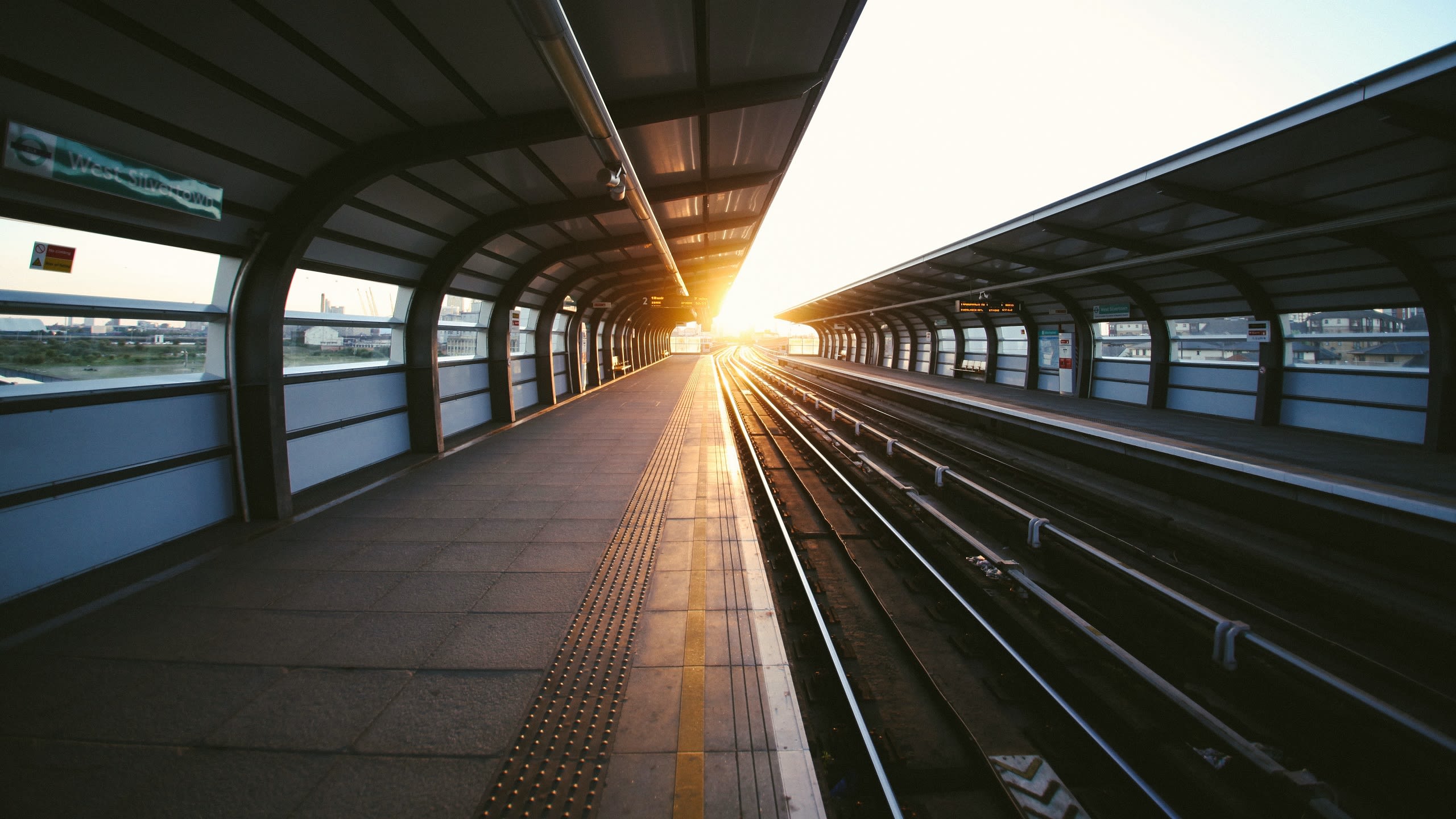 Looking down a train platform and railway line, with gentle sunlight shining on the horizon