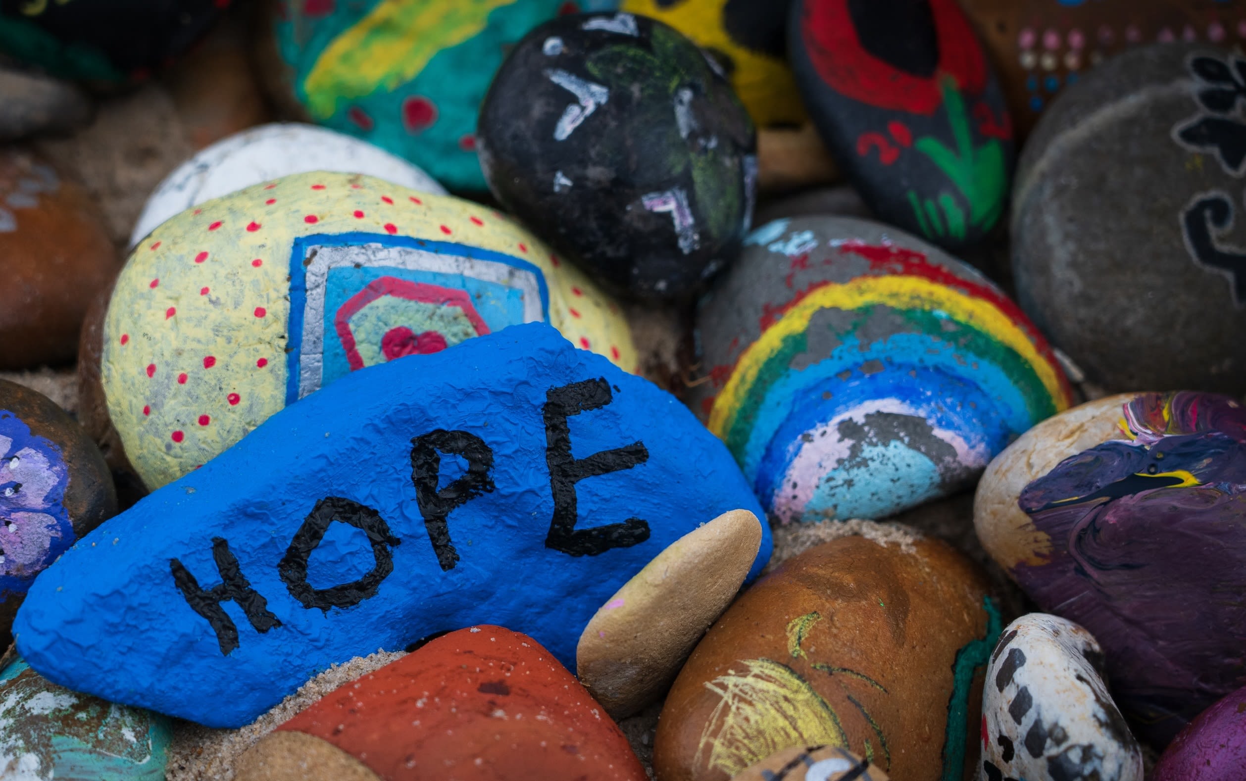 Hand painted stones painted in bright colours. One has a rainbow on and one says 'hope' on it